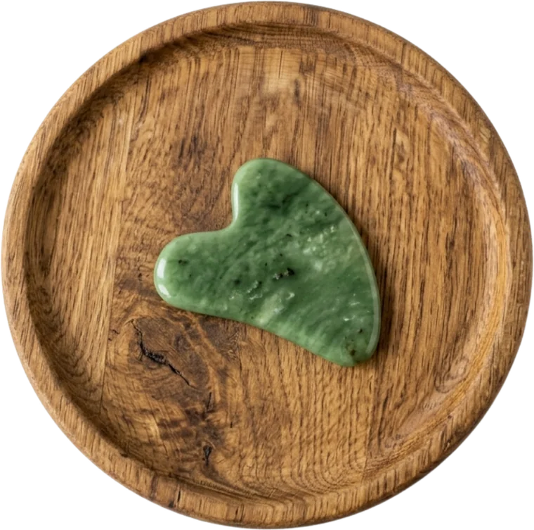 A jade gua sha tool resting on a wooden dish